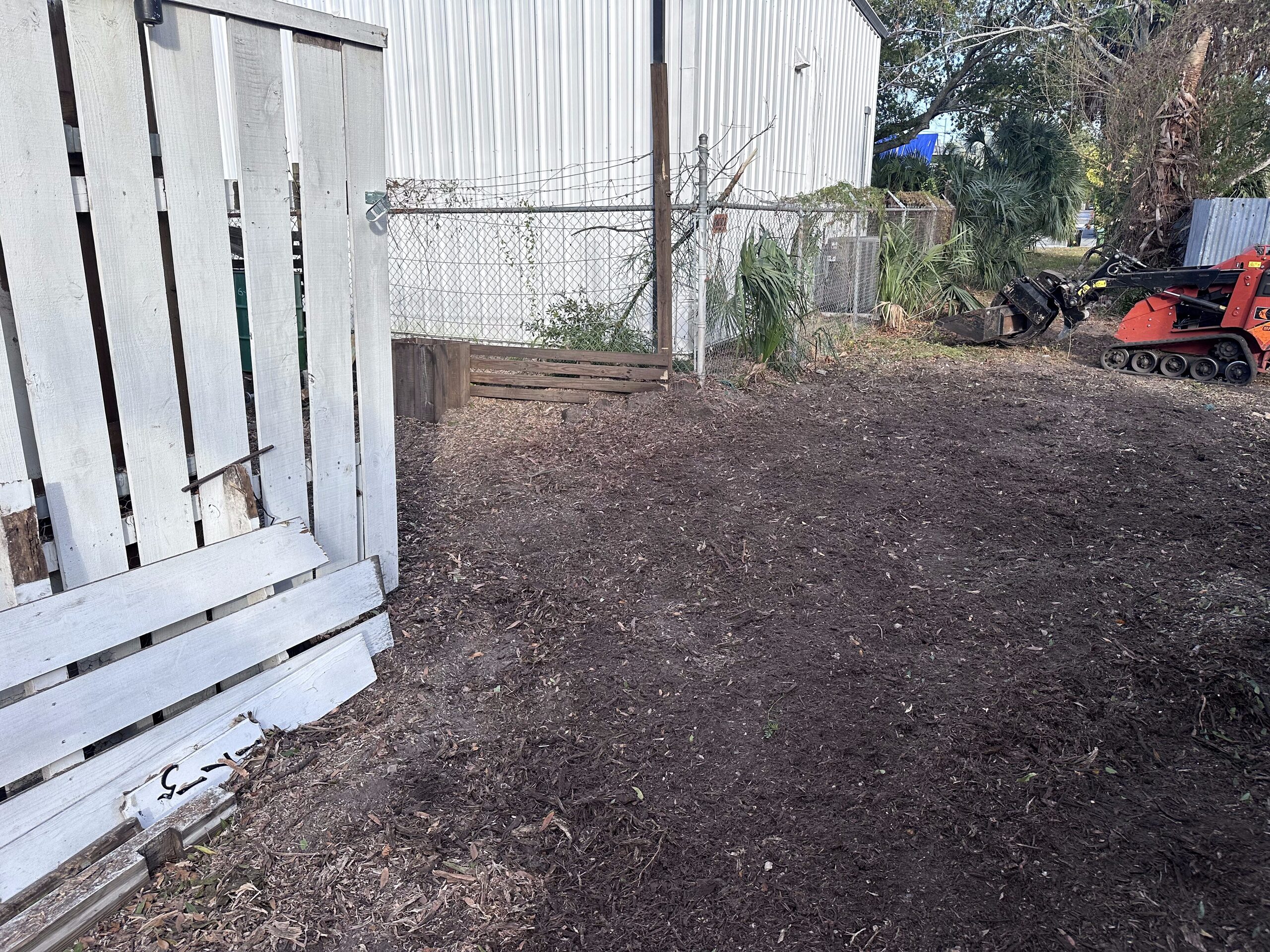 Tracked loader beside a cleared section of property after brush removal
